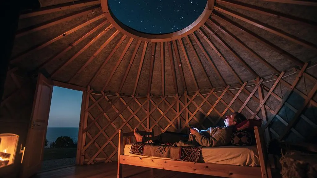 Intérieur chaleureux d'une yourte la nuit, avec vue sur le ciel étoilé à travers l'ouverture zénithale, non loin de la côte basque