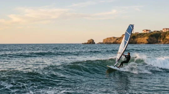 Véliplanchiste glissant sur une vague au large de la Côte des Basques à Biarritz, falaises basques en arrière-plan